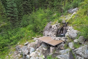 A wooden platform with a stone structure, surrounded by rocks and greenery. - Private Hot Spring | Views | River | Brundage (New Meadows)