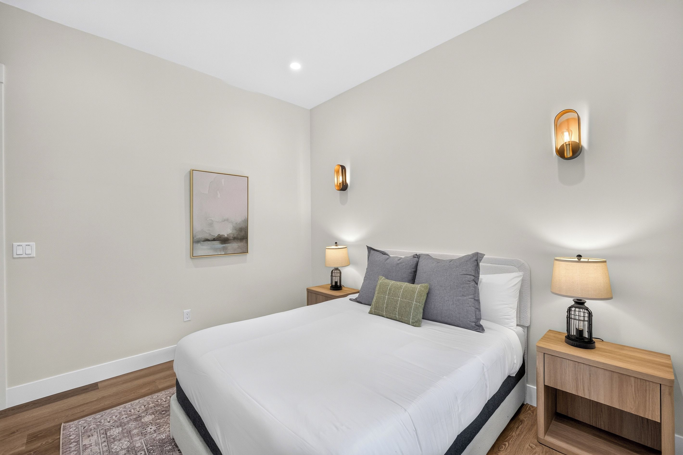 Un dormitorio con una cama grande, dos mesitas de noche con lámparas, una luz en la pared y un cuadro enmarcado.