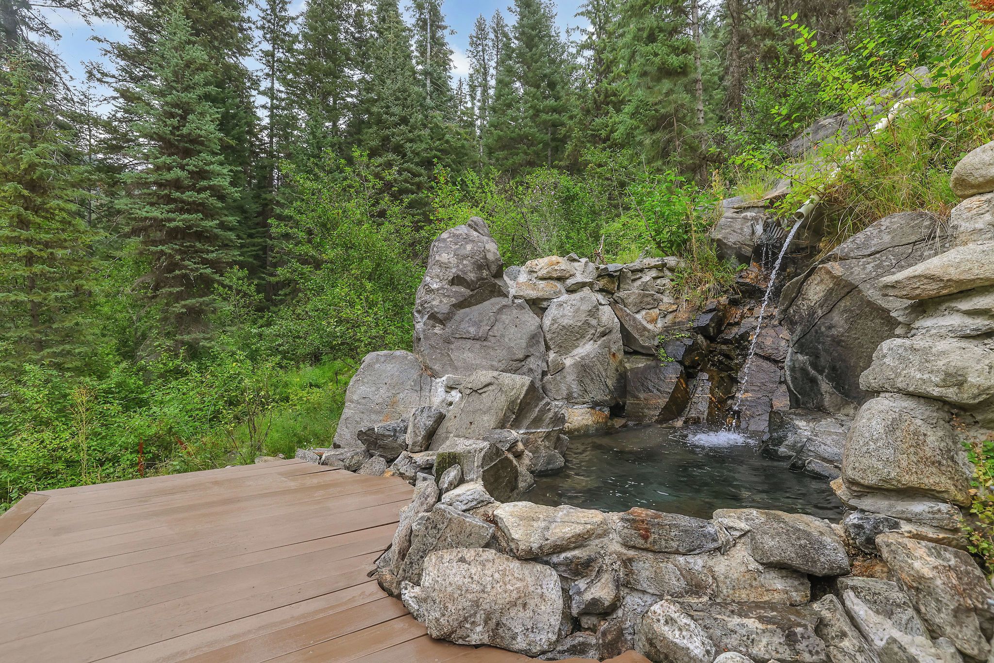 A wooden deck leading to a natural hot spring surrounded by rocks and dense forest.
