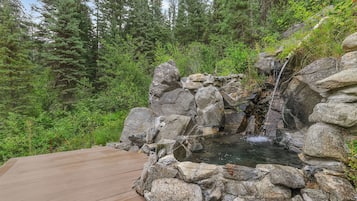 A wooden deck leading to a natural hot spring surrounded by rocks and dense forest.