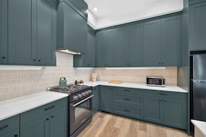 Una cocina con gabinetes color turquesa, estufa a gas, microondas y refrigerador.