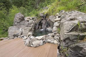 Una terraza de madera que lleva a un manantial termal natural rodeado de grandes rocas.