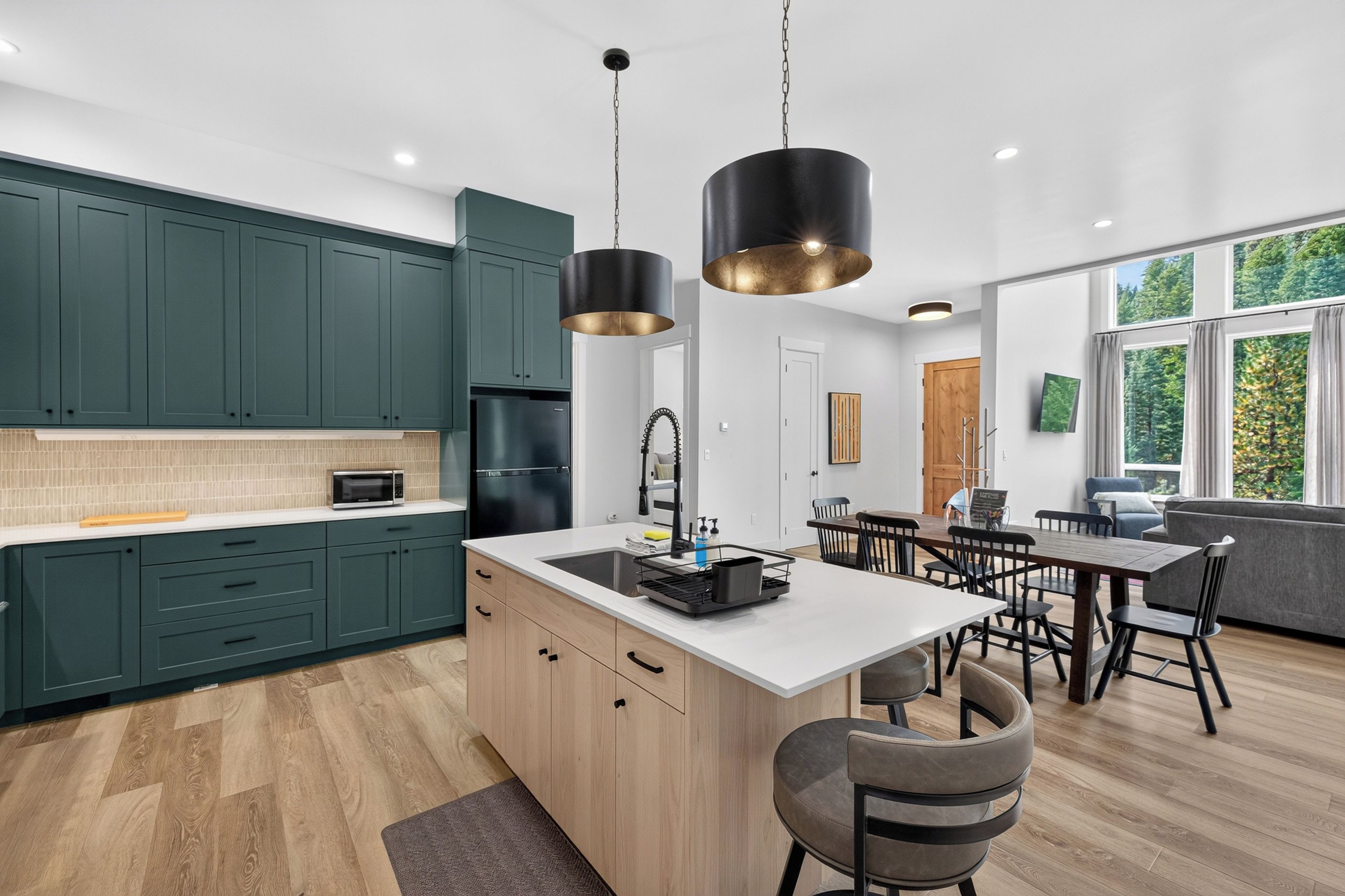 Cocina moderna con gabinetes verde oscuro, una isla central e iluminación colgante.