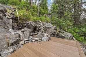 A wooden deck with a rocky landscape and dense forest in the background. - Private Hot Spring | Views | River | Brundage (New Meadows)