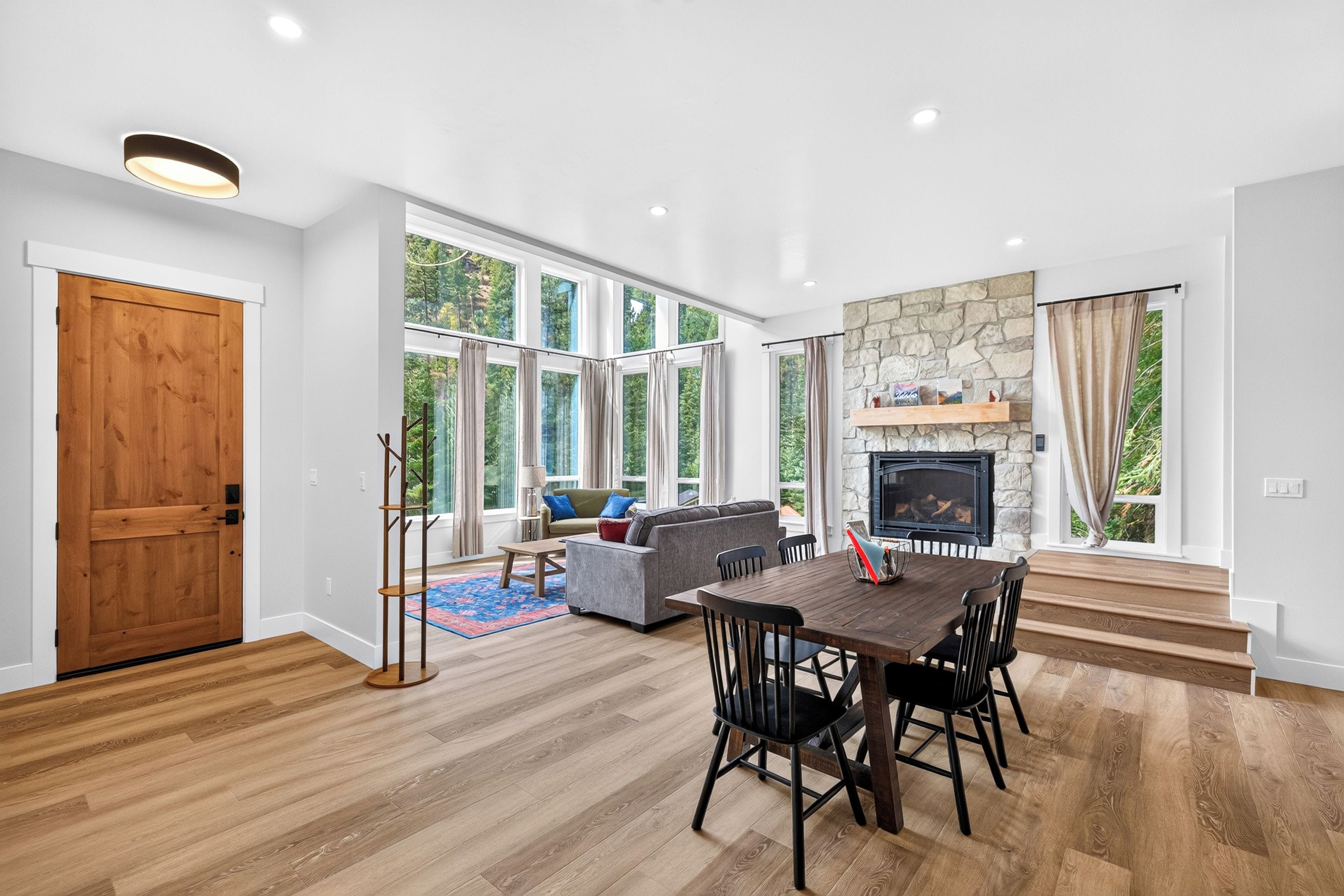 A spacious living room with a fireplace, large windows, and a dining area with a wooden table and chairs.