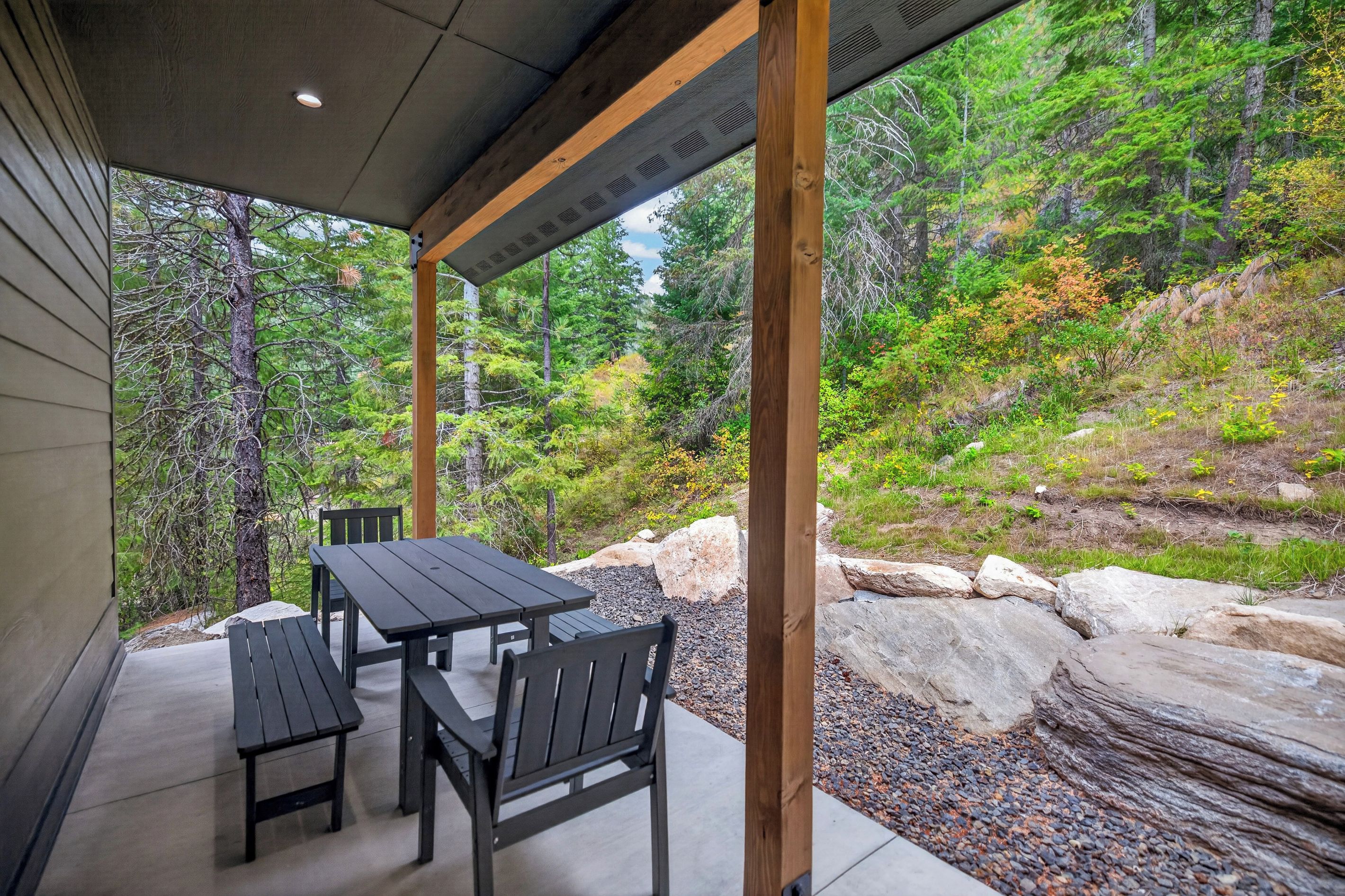 Un patio al aire libre con una mesa y sillas, rodeado de un paisaje natural con árboles y rocas.