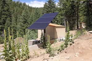 A small cabin with a solar panel roof, surrounded by a forested area. - Private Hot Spring | Views | River | Brundage (New Meadows)