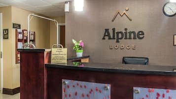 Mostrador de recepción en Alpine Lodge con un reloj, un cartel sobre recompensas y un florero.