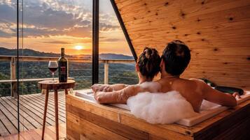 A couple relaxing in a wooden hot tub with a sunset view.