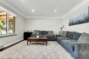 Un salon avec une grande fenêtre, un ensemble de canapés, une table basse et un tableau accroché au mur.