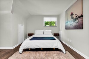 Ein Schlafzimmer mit Bett, Fenster, Gemälde und Tür.