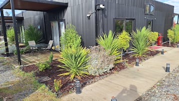 Un edificio moderno con un patio cubierto, mobiliario exterior y diversas plantas.