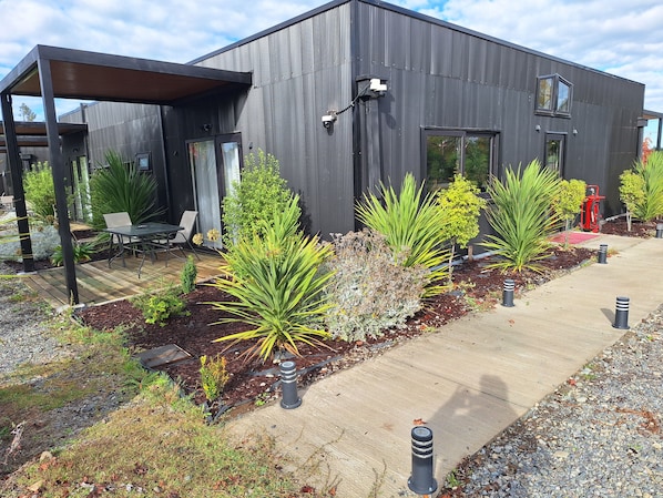 A modern building with a covered patio area, outdoor seating, and a variety of plants.