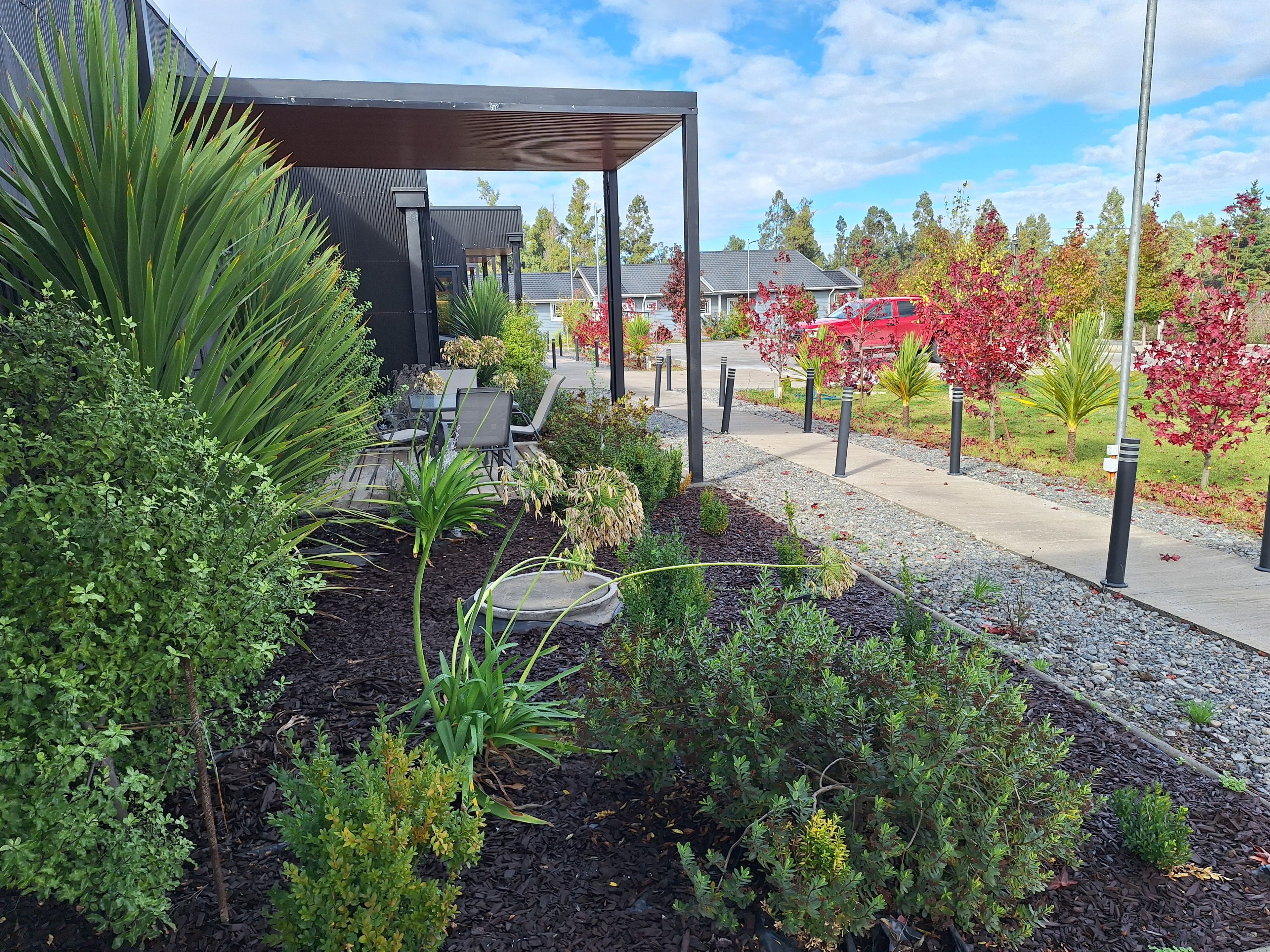 An outdoor seating area with a covered patio, surrounded by landscaped gardens and trees with autumn foliage.