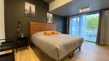 A bedroom with a large bed, a nightstand, a wall-mounted lamp, and two framed pictures.