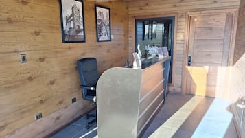 Un área de recepción con paneles de madera, un mostrador de recepción, una silla de oficina negra y cuadros enmarcados en la pared.