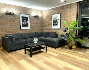 A modern living room with a sectional sofa, a coffee table, and two framed pictures on a brick wall.