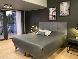 Un dormitorio moderno con una cama grande, cabecera, mesita de noche con lámpara y un cuadro en la pared.