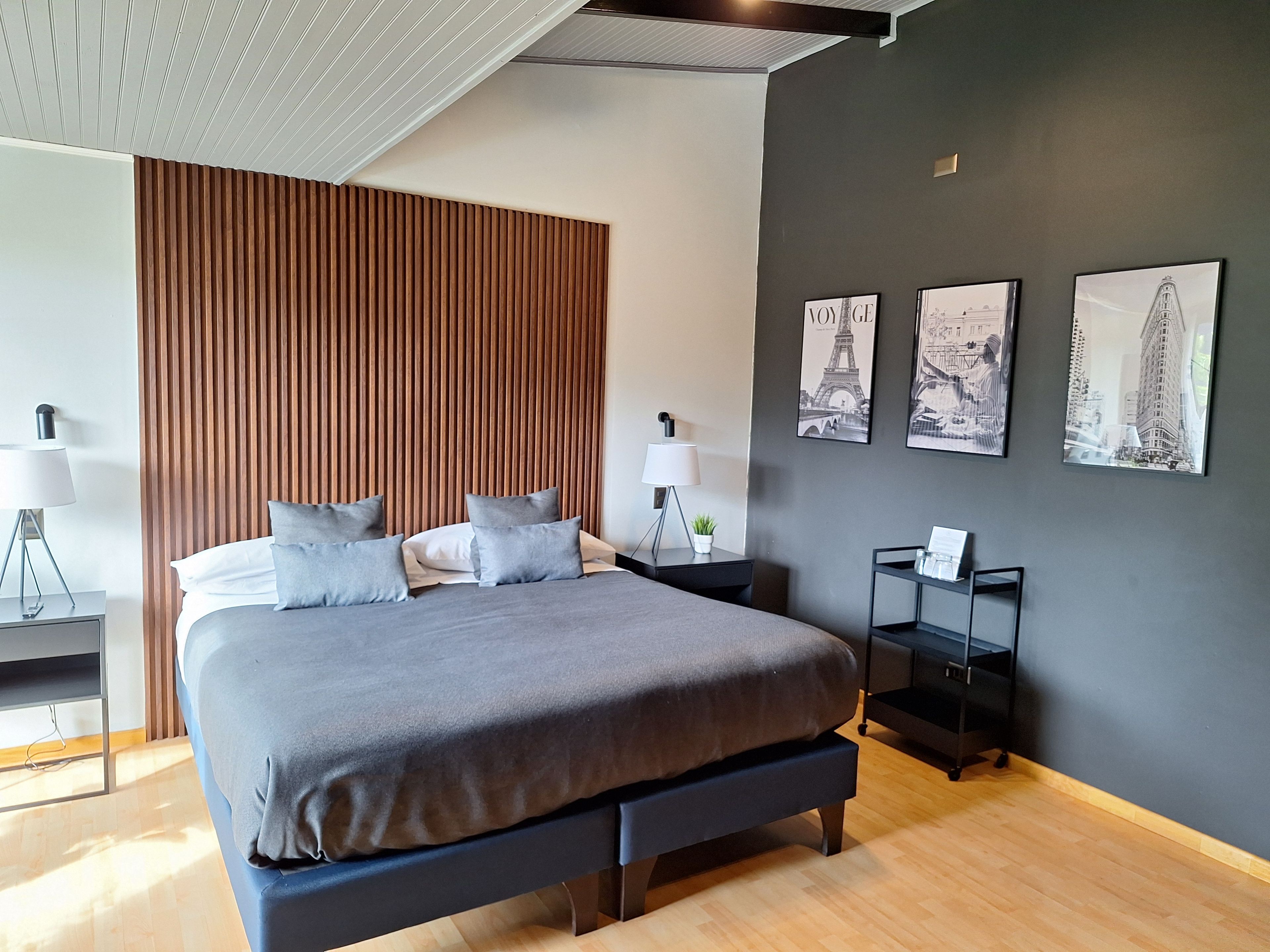 Une chambre moderne avec un grand lit, une tête de lit en lattes de bois et trois tableaux encadrés accrochés au mur.