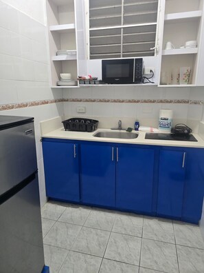 Een keuken met blauwe kastjes, een roestvrijstalen koelkast, een magnetron en een spoelbak.