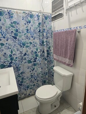 Een badkamer met een wit toilet, een douchegordijn met een patroon van zeedieren en een paarse handdoek aan de muur.