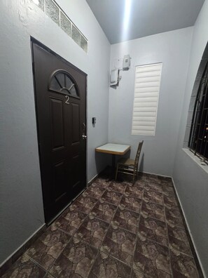 A narrow hallway with a dark door, a small table, and a chair.