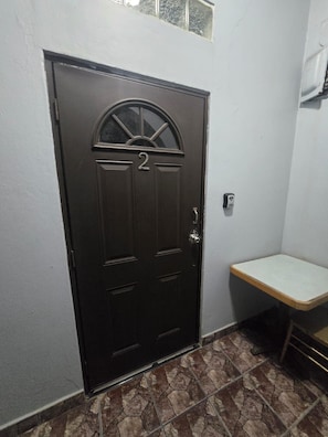 Una porta marró fosc amb el número 2, una petita finestra a dalt i una prestatgeria blanca a la dreta.