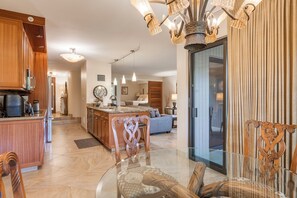 Eine moderne Küche mit Kochinsel, ein Essbereich mit Glastisch und ein Wohnbereich mit Sofa und Fernseher.