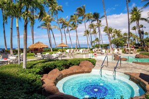A pool area with lounge chairs, palm trees, and a view of the ocean. - 160 Steps from kitchen sink to sand! Platinum Interior. 1431sf - New Ownership! (Lahaina)