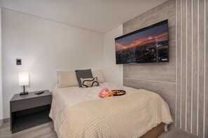 Une chambre à coucher moderne avec un lit, une table de chevet, un téléviseur et une vue sur le paysage urbain.