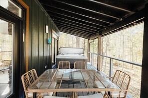 A covered outdoor seating area with a hot tub, wicker chairs, and a glass table.