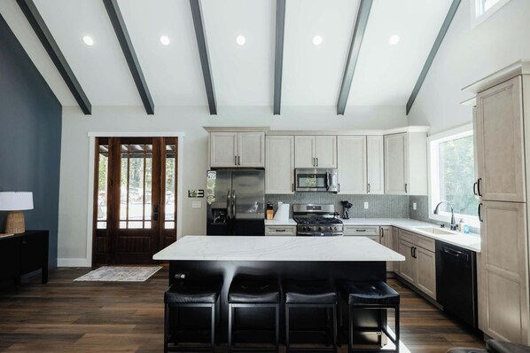 A modern kitchen with a central island, stainless steel appliances, and a herringbone tile backsplash.