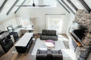 A modern kitchen with a central island, a dining area with a sofa and a coffee table, and a stone fireplace.
