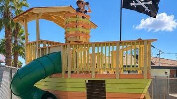 A play structure with a slide, a lookout tower, and a pirate flag.