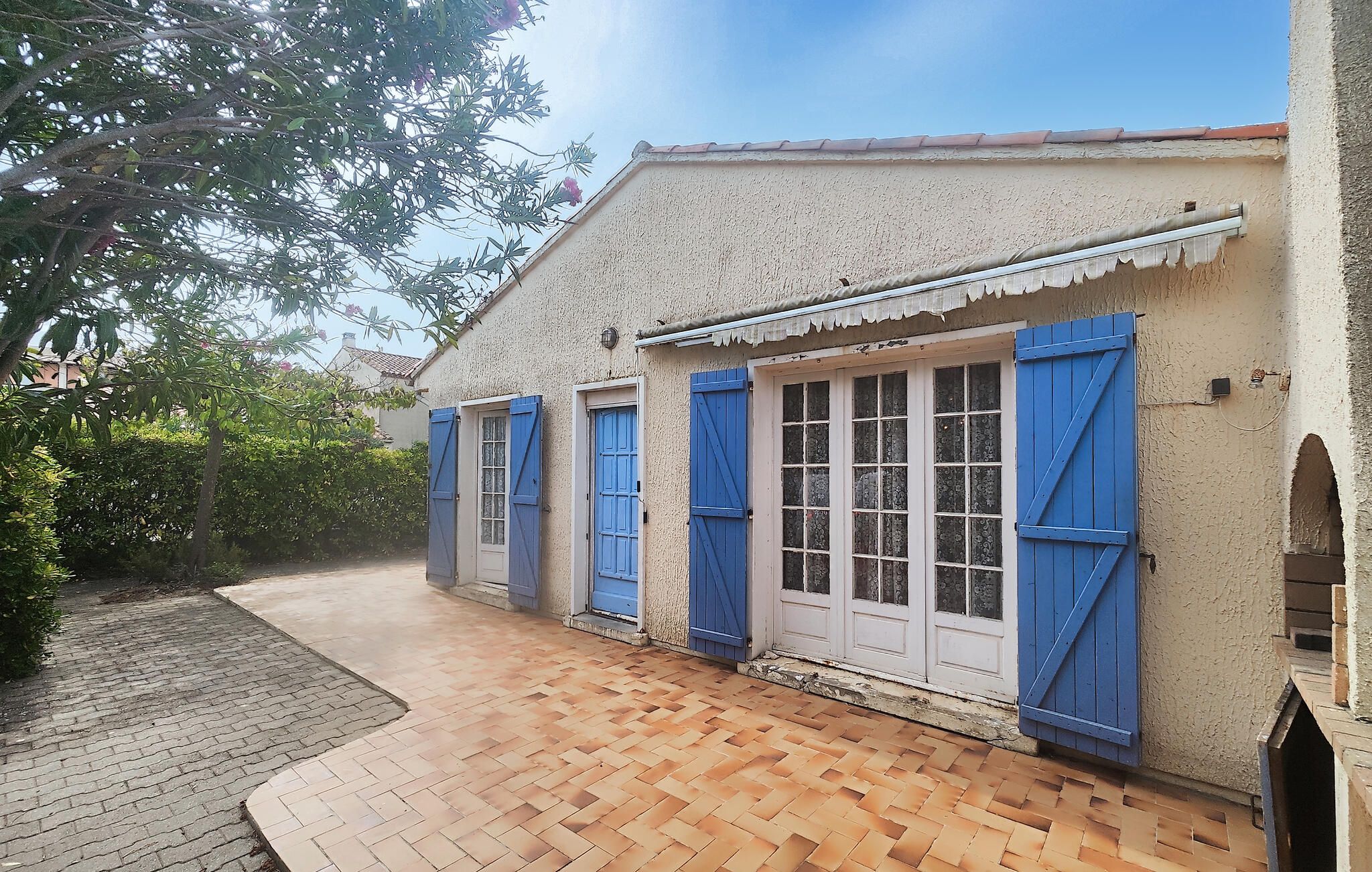 A building with a tiled roof, a paved entrance, and a window with blue shutters.