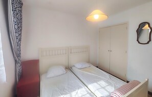 A single bed with a white headboard and two pillows, a bedside table with a striped pillow, a hanging lamp, and a wardrobe. - Beautiful home in Valras Plage with WiFi (Valras Plage)