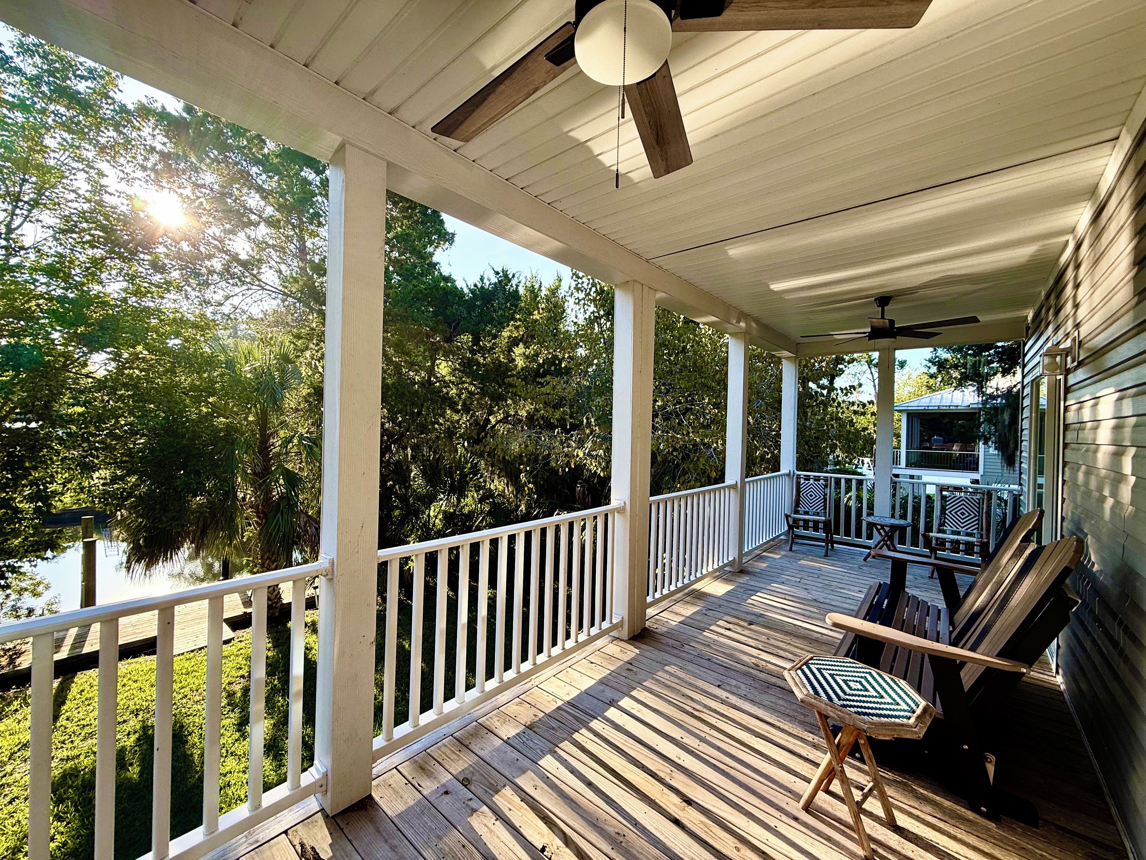 A covered porch with a railing, wooden deck, and a ceiling fan.