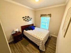 A bedroom with a bed, a nightstand, a lamp, a window with a view, and a wall decoration. - Diggs on the River (crystal River)