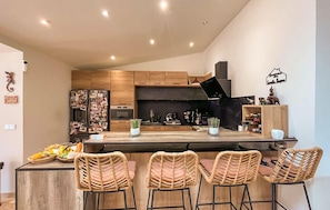 A modern kitchen with wooden cabinets, a black countertop, and a central island with bar stools. - Nice home in Le Val with private swimming pool, can be inside or outside (Le Val)