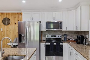 A modern kitchen with white cabinets, stainless steel appliances, a granite countertop, and a wooden wall. - Arrowhead Hideaway Hot Tub Fire Pit Game Room (Monroe County)