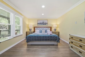 A bedroom with a bed, bedside tables, a dresser, a window with blinds, and a painting on the wall. - Arrowhead Hideaway Hot Tub Fire Pit Game Room (Monroe County)
