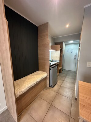 A narrow hallway with a bench, a refrigerator, and a door leading to a room. - Monoambiente céntrico sobre calle Mitre (San Carlos de Bariloche)