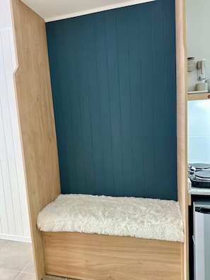 A corner of a room with a wooden bench, a teal-colored wall, and a white fluffy rug. - Monoambiente céntrico sobre calle Mitre (San Carlos de Bariloche)