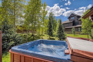 A hot tub in a backyard with a wooden deck, surrounded by trees and a house in the background. - Beautiful 3 Bedroom + Den Townhome in Breckenridge, Colorado (Breckenridge)