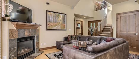 A spacious living room with a fireplace, a large sectional sofa, and a flat-screen TV mounted above it.