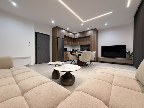 A modern living room with a sofa, a dining table, and a kitchen area with a TV.