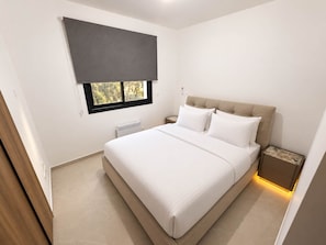 A modern bedroom with a large bed, a window with a blind, a bedside table, and a radiator.