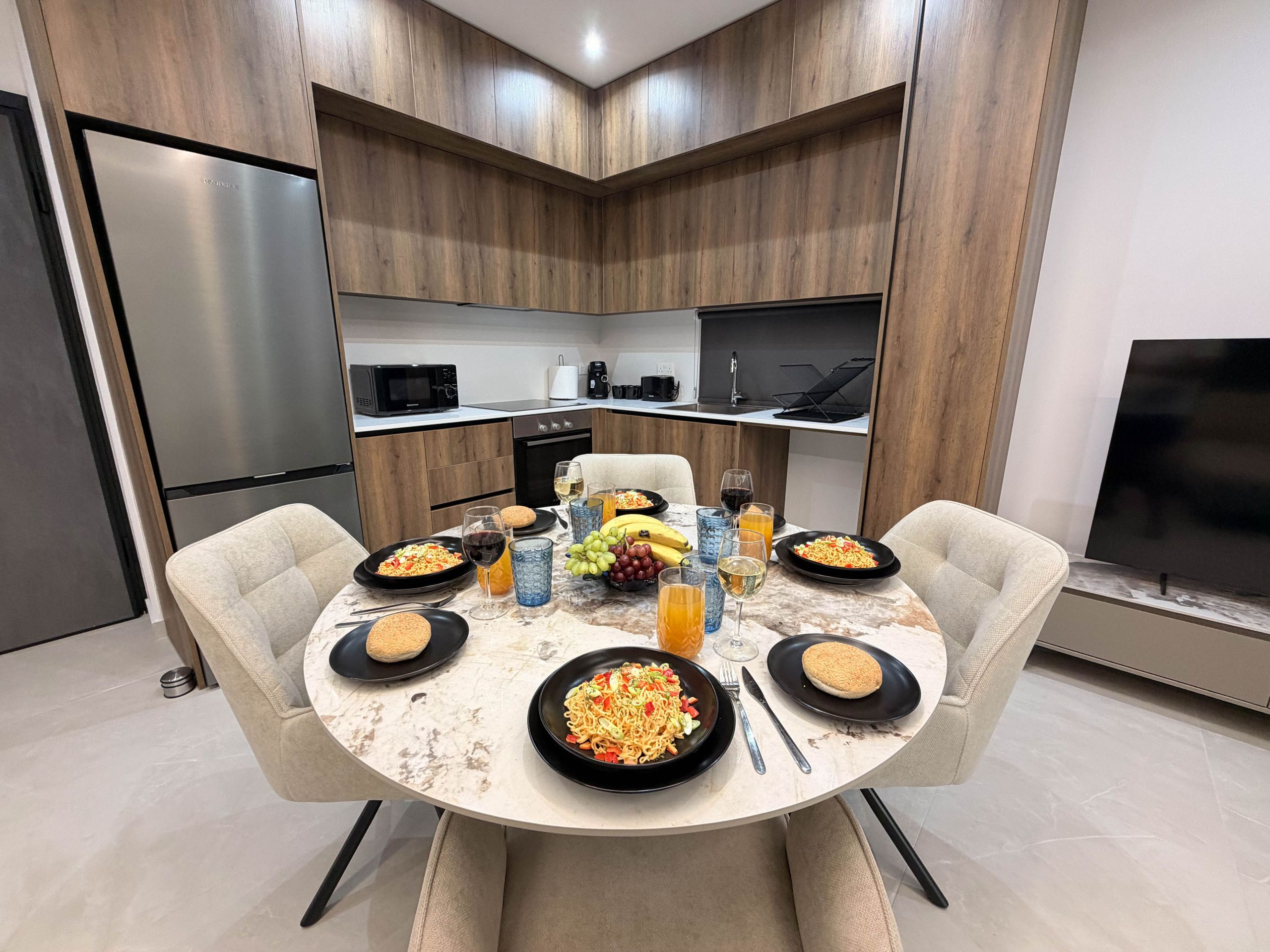 A modern kitchen with a dining table set for a meal, including plates of food, glasses, and a fruit bowl.