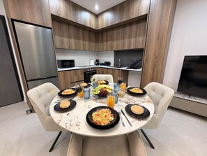 A modern kitchen with a dining table set for a meal, including plates of food, glasses, and a fruit bowl.