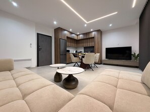 A modern living room with a sofa, a dining table, and a kitchen area with a TV.